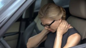 woman sitting in car in pain holding neck