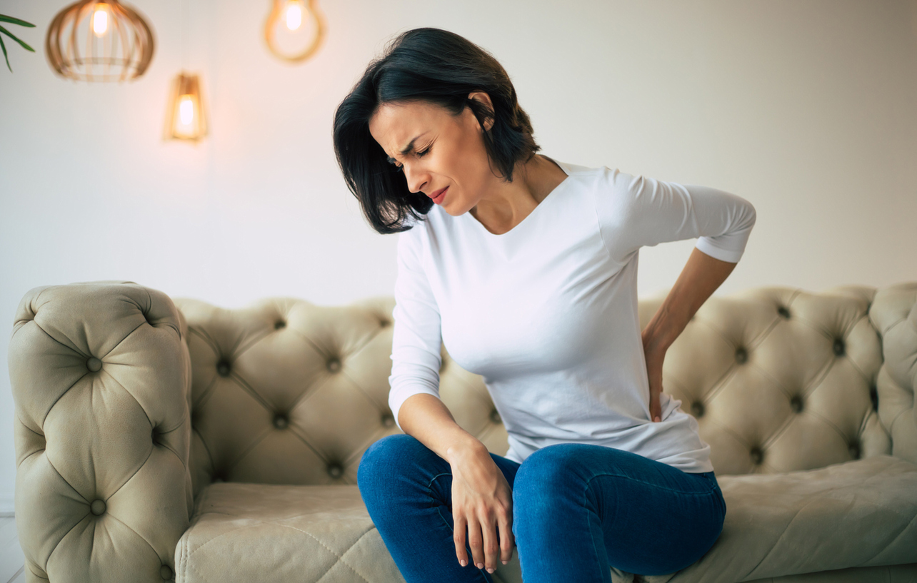 woman sitting on couch holding back in pain
