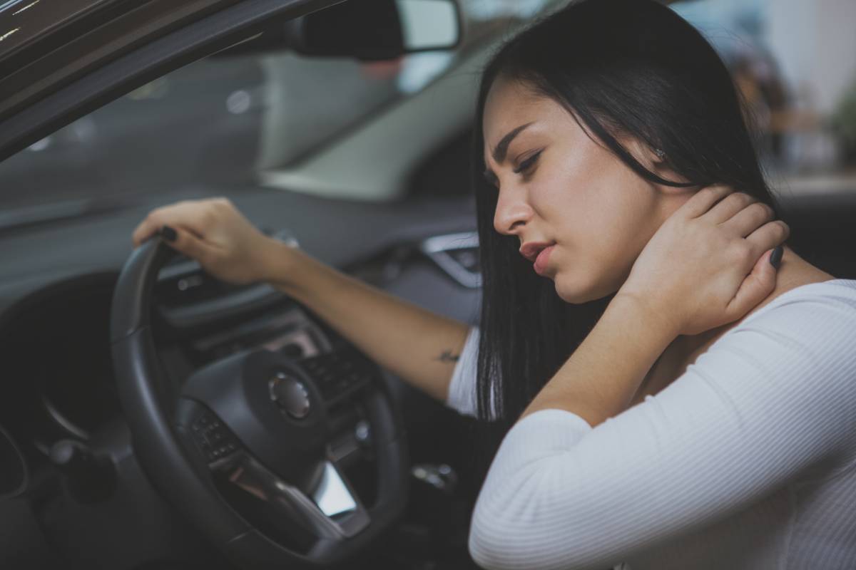 woman sitting in car holding neck in discomfort